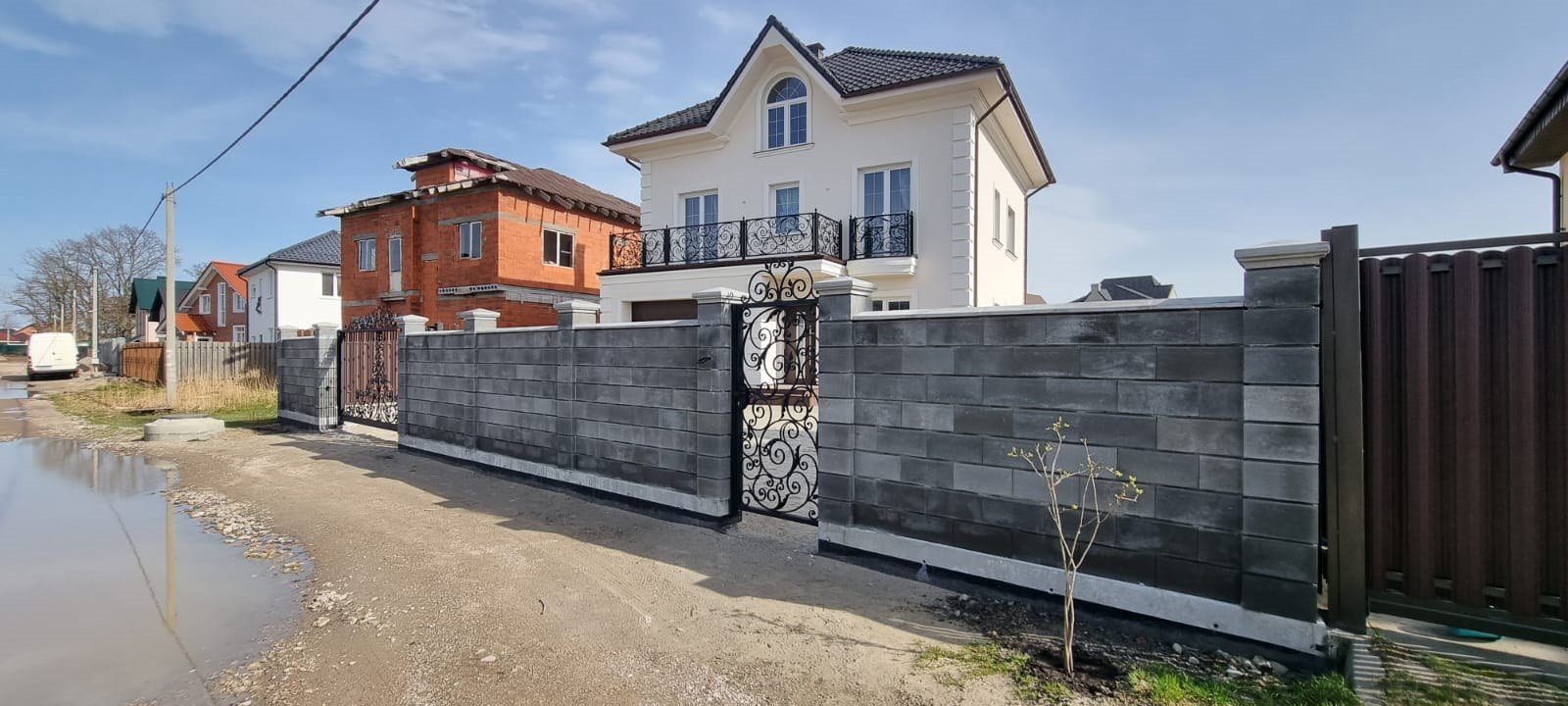 высокий забор избетонных блоков, столбы с оголовниками